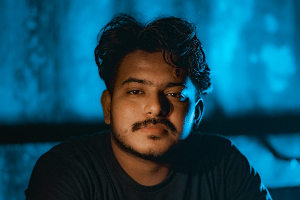 Close-up portrait of a young man with a thoughtful expression against a blue backdrop.